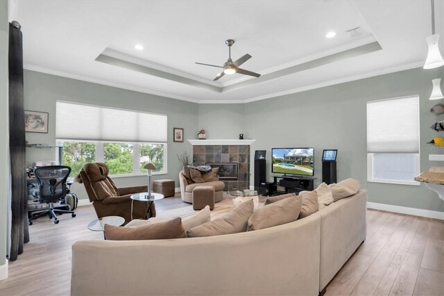 living room featuring light hardwood / wood-style floors, ceiling fan, a tray ceiling, and a fireplace