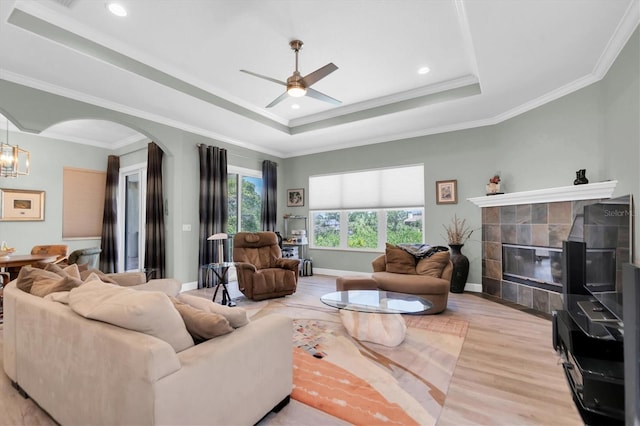 living area featuring arched walkways, a raised ceiling, crown molding, and a tile fireplace