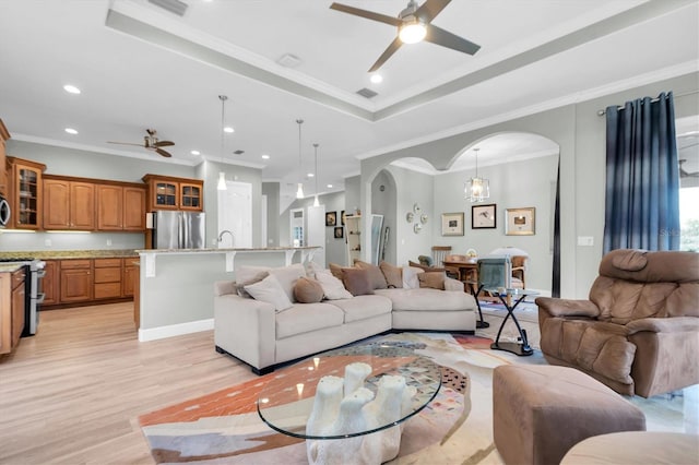 living room with light wood-style floors, a ceiling fan, arched walkways, and a tray ceiling