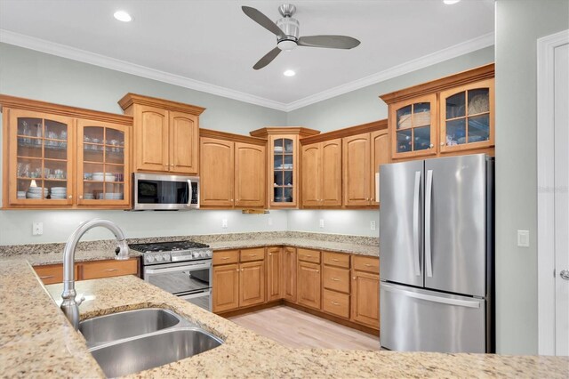 kitchen featuring glass insert cabinets, appliances with stainless steel finishes, ornamental molding, light stone countertops, and a sink