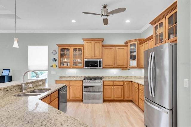 kitchen with glass insert cabinets, appliances with stainless steel finishes, ornamental molding, light stone countertops, and a sink