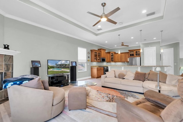 living room with a fireplace, a raised ceiling, visible vents, light wood-style flooring, and ornamental molding