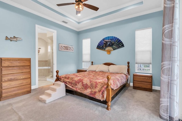 carpeted bedroom with a tray ceiling, crown molding, visible vents, ensuite bathroom, and baseboards