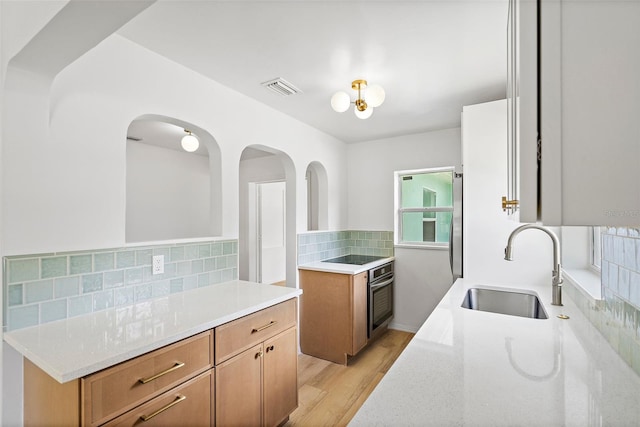 kitchen featuring light hardwood / wood-style flooring, backsplash, stainless steel oven, and sink