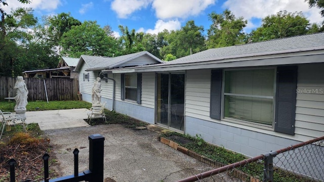 view of property exterior featuring roof with shingles, fence, and a patio