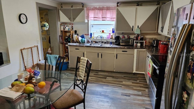 kitchen featuring a toaster, wood finished floors, a sink, appliances with stainless steel finishes, and dark countertops