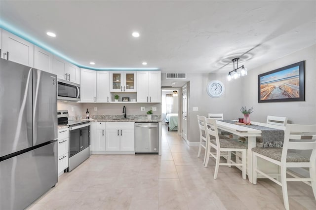 kitchen with light stone countertops, pendant lighting, appliances with stainless steel finishes, sink, and white cabinetry