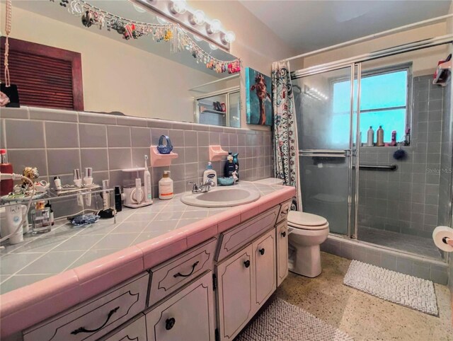 bathroom featuring vanity, toilet, tasteful backsplash, and a shower with door