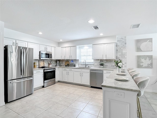 kitchen with stainless steel appliances, kitchen peninsula, sink, light stone countertops, and white cabinets