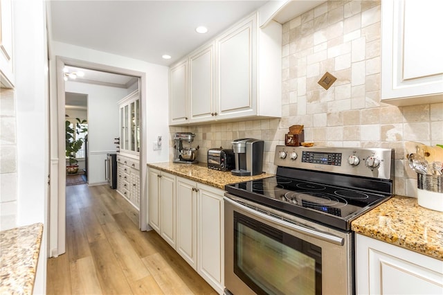 kitchen featuring light stone countertops, white cabinetry, light hardwood / wood-style flooring, and stainless steel electric range oven