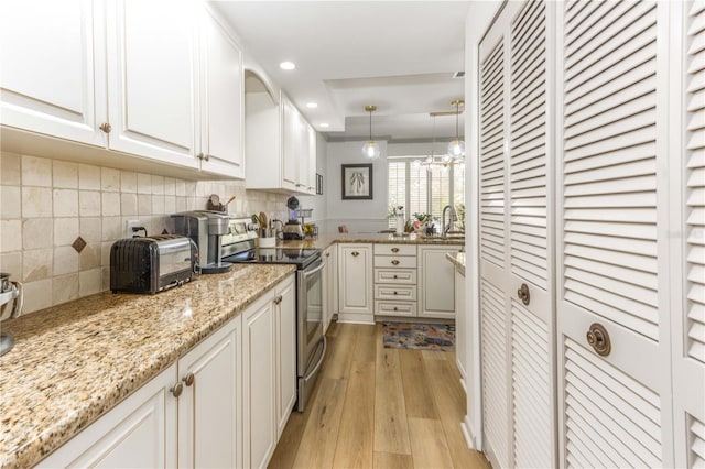 kitchen featuring decorative light fixtures, stainless steel range with electric cooktop, light wood-type flooring, white cabinetry, and light stone counters