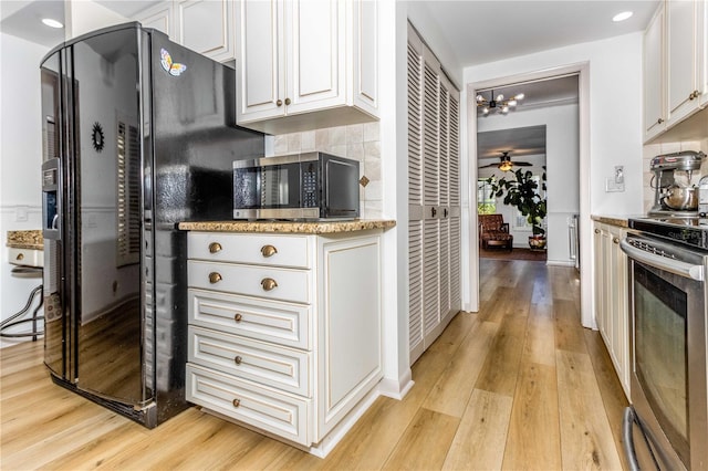 kitchen with stainless steel appliances, ceiling fan with notable chandelier, light stone countertops, white cabinets, and light hardwood / wood-style floors