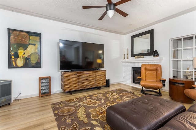 living room featuring wood-type flooring, crown molding, a brick fireplace, a textured ceiling, and ceiling fan