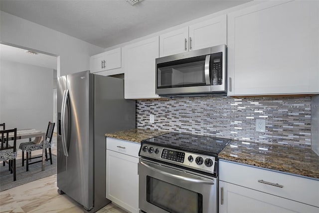 kitchen featuring dark stone counters, tasteful backsplash, stainless steel appliances, and white cabinets