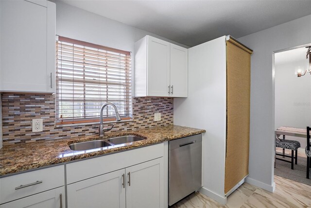 kitchen with stainless steel dishwasher, sink, dark stone counters, and white cabinets