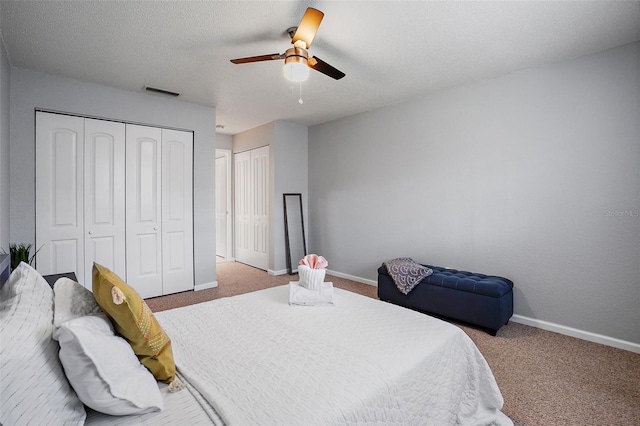 carpeted bedroom with multiple closets, a textured ceiling, and ceiling fan