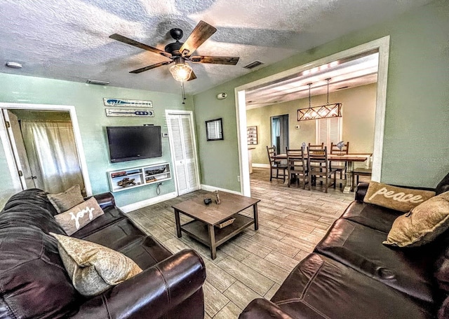 living room with a textured ceiling, ceiling fan, and light hardwood / wood-style floors