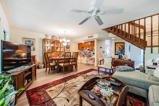 living room with a textured ceiling, ceiling fan with notable chandelier, and light hardwood / wood-style floors