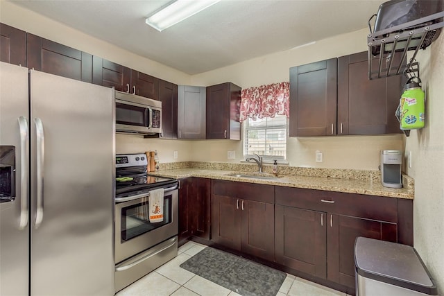 kitchen featuring appliances with stainless steel finishes, light tile patterned floors, sink, and light stone countertops