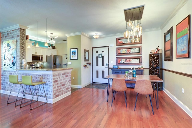 dining area with a notable chandelier, wood-type flooring, crown molding, and sink