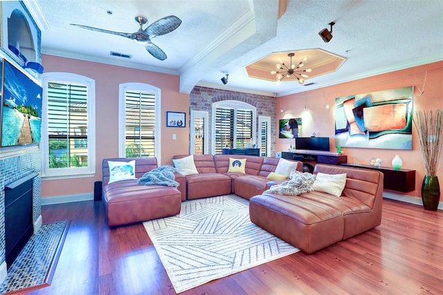 living room with hardwood / wood-style flooring, a fireplace, ceiling fan with notable chandelier, ornamental molding, and a textured ceiling