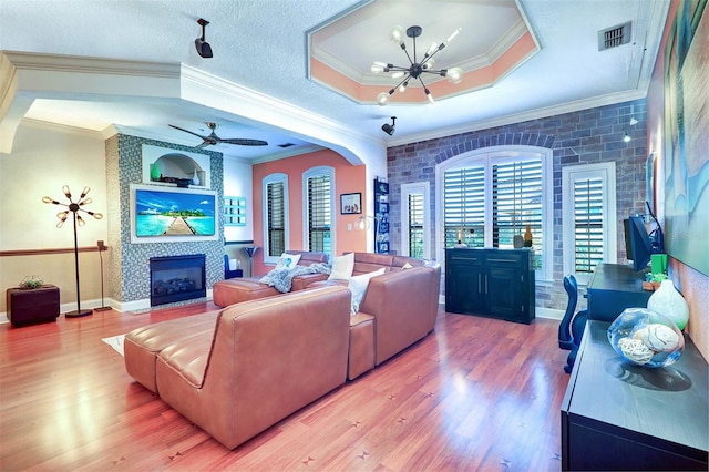 living room featuring ceiling fan with notable chandelier, ornamental molding, hardwood / wood-style floors, and a tile fireplace