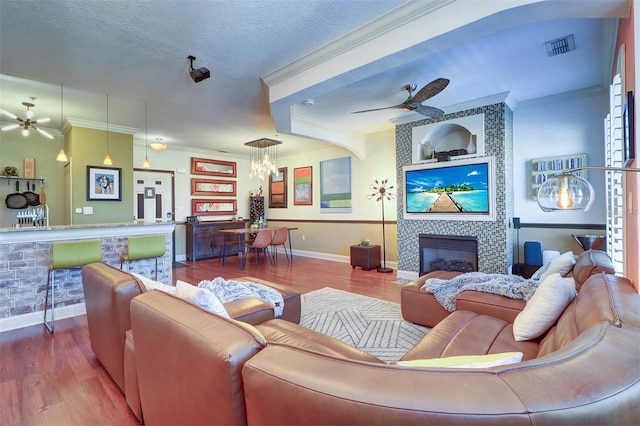 living room with ceiling fan with notable chandelier, hardwood / wood-style flooring, a tiled fireplace, and crown molding