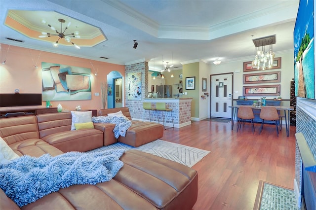 living room with wood-type flooring, a raised ceiling, a chandelier, and ornamental molding