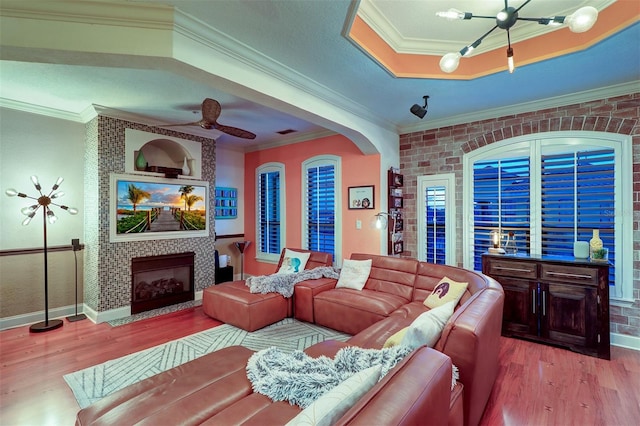 living room featuring a fireplace, ornamental molding, hardwood / wood-style flooring, and ceiling fan with notable chandelier