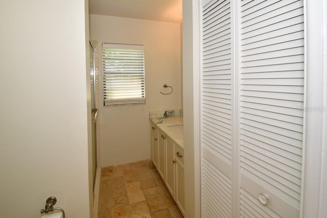 full bathroom featuring stone tile flooring, baseboards, walk in shower, and vanity