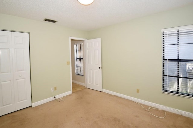 unfurnished bedroom featuring light carpet, baseboards, a closet, and a textured ceiling