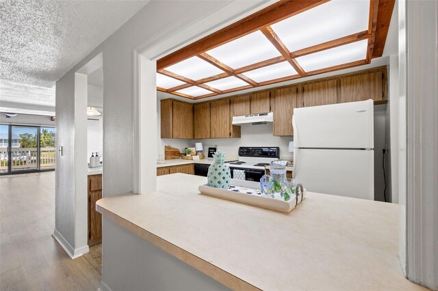 kitchen with a textured ceiling, range with electric stovetop, white fridge, and light wood-type flooring