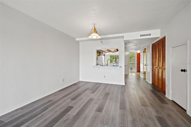 empty room with baseboards, visible vents, dark wood-type flooring, a textured ceiling, and a sink