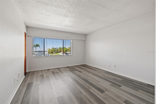 spare room with a textured ceiling, wood finished floors, and baseboards