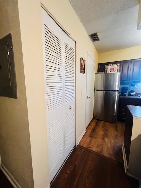 kitchen featuring stainless steel fridge, a textured ceiling, electric panel, and dark wood-type flooring