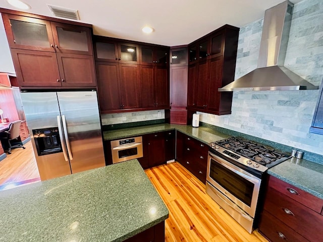 kitchen with wall chimney exhaust hood, stainless steel appliances, light hardwood / wood-style floors, and decorative backsplash