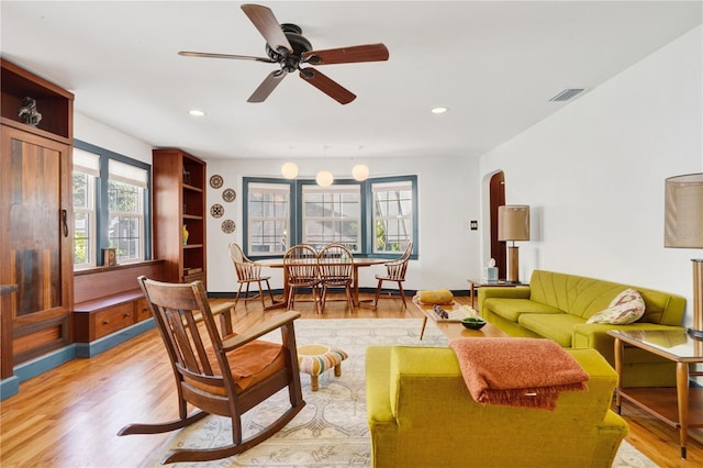 living room with ceiling fan with notable chandelier and light hardwood / wood-style flooring