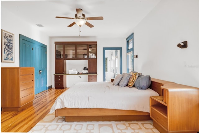 bedroom featuring ceiling fan, light hardwood / wood-style flooring, a closet, and ensuite bath