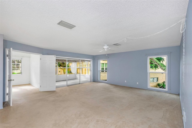 unfurnished living room featuring light colored carpet, a wealth of natural light, ceiling fan, and a textured ceiling