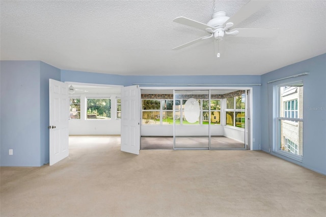 carpeted spare room with a textured ceiling, plenty of natural light, and ceiling fan