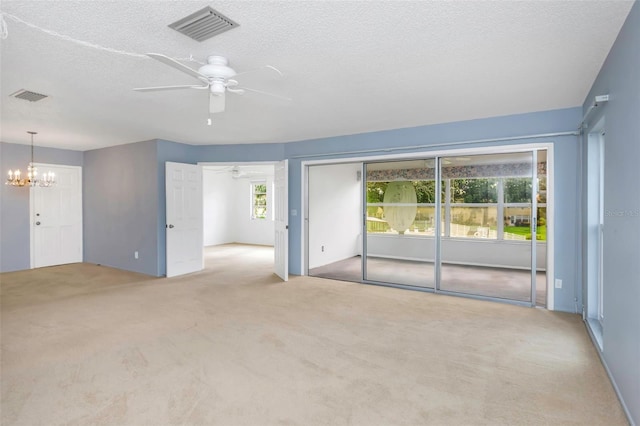 carpeted spare room with ceiling fan with notable chandelier and a textured ceiling