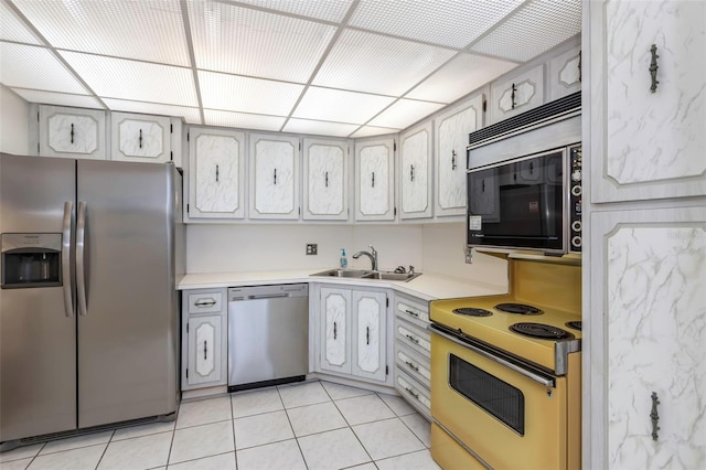 kitchen with a paneled ceiling, light tile patterned floors, stainless steel appliances, and sink