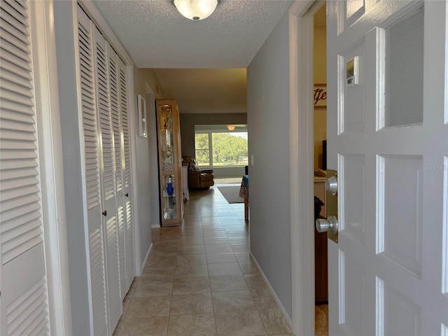 hall with a textured ceiling and light tile patterned flooring