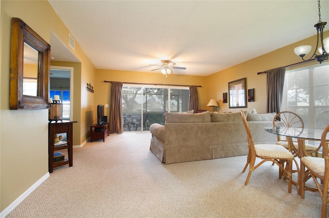 carpeted living room with ceiling fan with notable chandelier