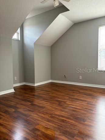 additional living space featuring lofted ceiling, ceiling fan, dark hardwood / wood-style flooring, and a textured ceiling