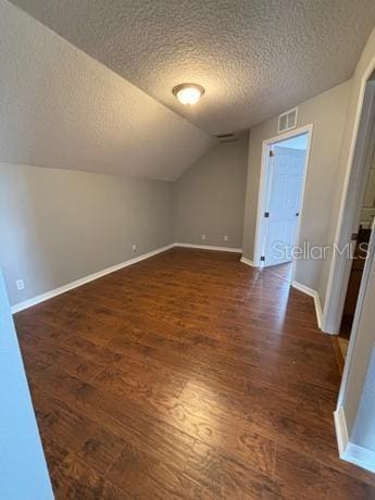 additional living space featuring a textured ceiling, dark wood-type flooring, and vaulted ceiling