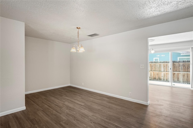 empty room with dark wood-type flooring, an inviting chandelier, and a textured ceiling