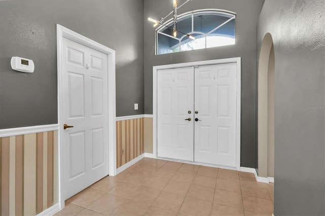 entryway featuring a wainscoted wall, baseboards, arched walkways, and light tile patterned flooring