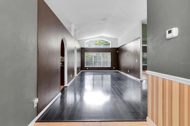 spare room with lofted ceiling, arched walkways, baseboards, and wood finished floors