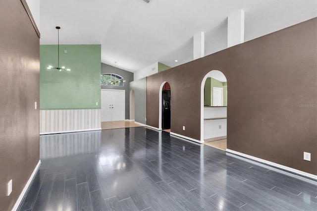 empty room with high vaulted ceiling, wood tiled floor, arched walkways, and an inviting chandelier